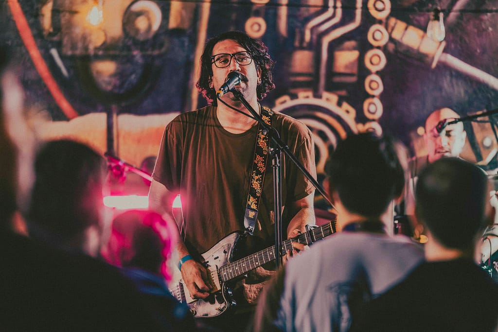Banda Los Martes interpretando rock alternativo en escenario de KUP, Centro Histórico de Mexicali. Fotografía de alta calidad, estética grunge con influencia editorial, realizada por Yasunari Murayama. Músicos en acción, guitarras eléctricas, batería y bajo. Escena con mural artístico de fondo y luces de concierto. Imagen perfecta para portafolio musical, prensa, y redes de la banda. Evento cultural en Baja California, fotografía artística de rock en vivo, capturas documentales para promoción de grupos independientes. Estilo moderno, colores intensos, fotografía con Canon R6, imagen para cartel de rock, captura de momentos icónicos en el escenario.
