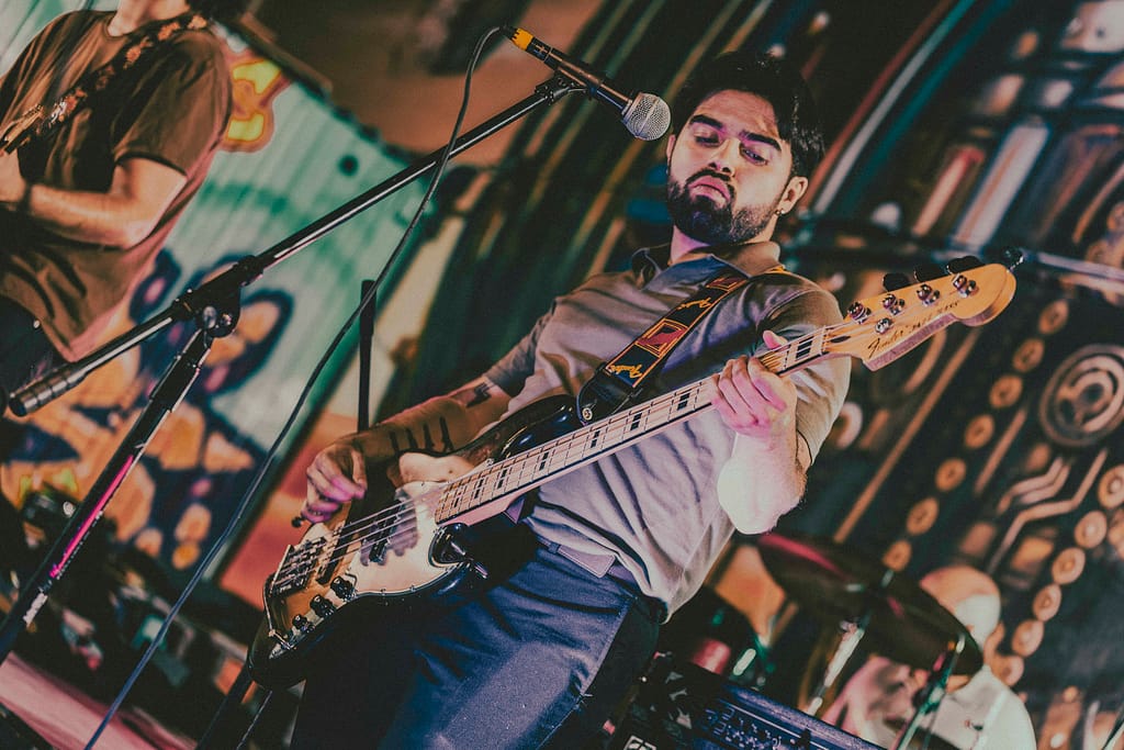 Concierto de Los Martes en vivo en KUP, Mexicali, Baja California. Foto de guitarrista tocando con energía, estilo grunge y estética de revista rockera. Fotografía profesional capturada por Yasunari Murayama con Canon R6, luces cálidas y fondo de mural artístico. Imagen ideal para medios musicales y redes sociales de la banda. Documental de música en vivo, evento cultural en el centro histórico de Mexicali. Rock alternativo, escena independiente, fotografía de espectáculo en vivo, retrato de músico en concierto, ambiente bohemio, estilo visual cinematográfico, fotografía editorial para promoción musical, foto para prensa cultural y agenda de eventos. productor de video en mexicali yasunari murayama