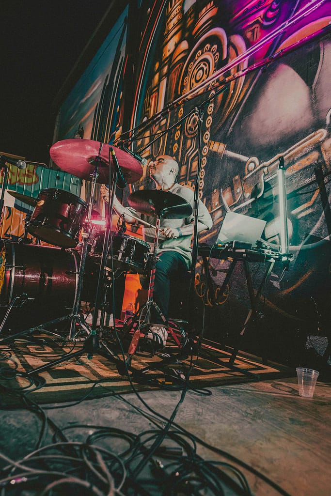 Concierto de Los Martes en vivo en KUP, Mexicali, Baja California. Foto de guitarrista tocando con energía, estilo grunge y estética de revista rockera. Fotografía profesional capturada por Yasunari Murayama con Canon R6, luces cálidas y fondo de mural artístico. Imagen ideal para medios musicales y redes sociales de la banda. Documental de música en vivo, evento cultural en el centro histórico de Mexicali. Rock alternativo, escena independiente, fotografía de espectáculo en vivo, retrato de músico en concierto, ambiente bohemio, estilo visual cinematográfico, fotografía editorial para promoción musical, foto para prensa cultural y agenda de eventos.