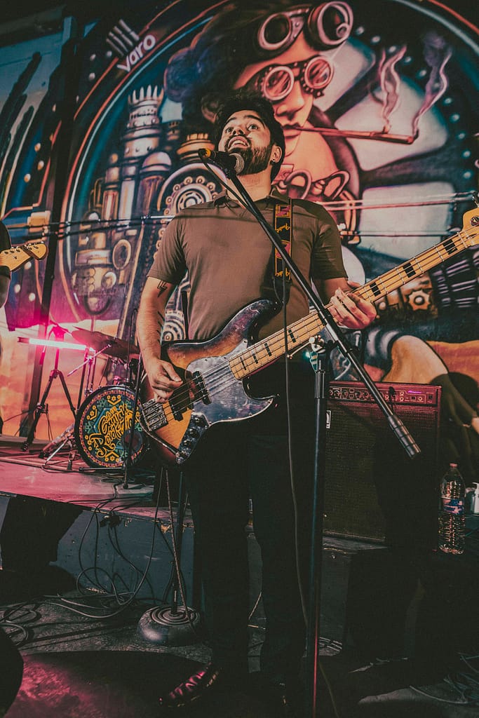 Fotografía profesional de la banda de rock Los Martes en concierto en KUP, Centro Histórico de Mexicali, Baja California. Imagen con estilo editorial y estética rockera grunge, capturada por el fotógrafo Yasunari Murayama con cámara Canon R6. Escenario decorado con arte urbano, luces de concierto, público disfrutando la música en vivo. Ideal para portadas de revista musical y documental de eventos. Fotografía artística de banda independiente en Mexicali, foto de guitarrista en escena, ambiente nocturno, rock alternativo, cultura musical local, músicos tocando en vivo, show energético, fotografía para promoción de bandas, imagen para cartel de concierto, retrato de rock en acción.